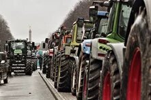 Photo: Tractors stand in a long row on the street in Berlin, with the Berlin Victory Column in the background and a sign with a protest message in front.
