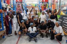 Mehrere Menschen stehen in einem Lagerraum und jubeln in die Kamera. 