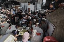 Viele Menschen mit Töpfen drängen sich vor großen Töpfen, aus denen Helfer*innen Suppe schöpfen (Gaza Soup Kitchen).