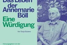 Ältere Frau mit hellem Haar sitzt auf Bank vor Blattwerk. Links Text: „Das Leben der Annemarie Böll – Eine Würdigung“ (The Life of Annemarie Böll – A Tribute).