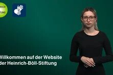 Person vor grünem Hintergrund, links Logos und Schrift der Böll-Stiftung.