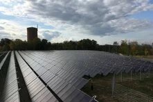 Großflächige Solarthermieanlage mit Reihen geneigter Kollektoren, im Hintergrund Bäume, ein Turm und Baukräne.