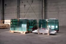 Mehrere große Glasplatten stehen auf Paletten in einer leeren Lagerhalle, teils mit Folie umwickelt.