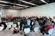 Über 50 Personen sitzen im Stuhlkreis in einem modernen Raum und hören einer Diskussion zu. Zwei Personen sprechen mit Mikrofon.