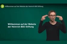 Frau gebärdet Video: Willkommen auf der Website der Heinrich-Böll-Stiftung. Startseite des Videos in Gebärdensprache. 