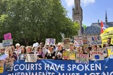 A group of people hold protest signs and a large banner in front of the International Court of Justice in The Hague, banner reads: "COURTS HAVE SPOKEN – GOVERNMENTS MUST ACT NOW"