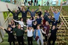 Gruppe von etwa 20 Personen auf Treppe, viele mit erhobenen Armen, lachend, teils in Bewegung.