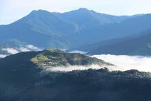 Built-up hillside in morning light, clouds drifting through the valley, tall forested mountains in the background.