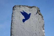 A concrete slab with a blue dove painted on it, broken at the top with exposed metal, set against a blue sky.