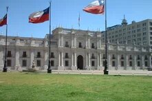 Foto des Präsidentenpalastes "La Moneda" in Santiago de Chile mit Vorplatz und Fahnenstangen mit gehisster chilenischer Flagge.