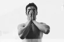 A man with a bare chest buries his face in his hands.