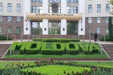 Vor dem Parlamentsgebäude der Republik Moldau steht in Buchsbaum das Wort „MOLDOVA“. Davor Blumenbeete, zwei Personen auf den Treppen.