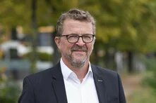 hbs Bildbeschreiber sagte:  Person mit Brille steht draußen vor unscharfem Hintergrund mit Bäumen und Wegen.