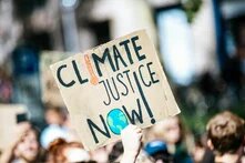 hbs Bildbeschreiber sagte:  Pappschild mit Aufschrift „Climate Justice Now!“ (Klimagerechtigkeit jetzt!) wird von Mensch in Menschenmenge hochgehalten.