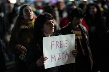 Person hält ein Schild mit der Aufschrift „FREE MZIA!“ in einer Menschenmenge bei Dunkelheit.