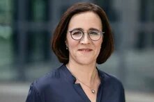 Person mit Brille steht draußen vor unscharfem Hintergrund und blickt leicht lächelnd in die Kamera.