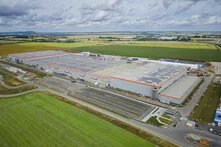 Large industrial building with solar panels on the roof, surrounded by fields, roads, and mostly empty parking lots.