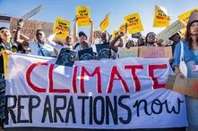 Gruppe von Aktivist*innen hält Banner mit „Climate Reparations now“ und Schildern wie „Show us the money“.