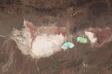 Bright salt flats with straight lines, turquoise-green basins for lithium mining on the right in a dry mountain landscape.