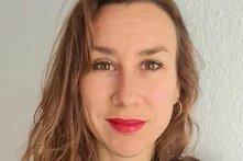 Person mit offenen Haaren blickt in Innenraum frontal in die Kamera und lächelt leicht.