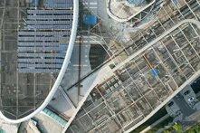 Aerial view of a curved building under construction with solar panels and a grid-like roof structure.