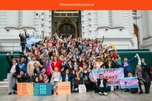 Large group of people in front of a house holding up various signs with Spanish inscriptions.
