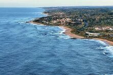 Coastline with a few villages on the right, sea on the left, sandy beaches, and scattered rocks along the shore.