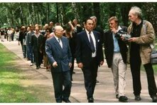 Gruppe geht auf einem Waldweg, vorne vier Personen im Gespräch, eine hält eine Kamera, viele folgen im Hintergrund.