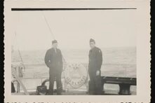 Zwei Personen in Uniform stehen an Deck vor Rettungsring mit Aufschrift „U.S.A.T. Gen. R. L. Howze“, Meer im Hintergrund.