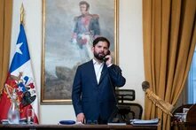 Ein Mann steht telefonierend an einem Schreibtisch, hinter ihm ein Gemälde und eine chilenische Flagge.