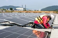 Eine Person kniet zwischen Solarpaneelen und arbeitet mit Werkzeug auf einer schwimmenden Plattform.