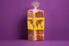 Ein in Plastik verpacktes, vorgeschnittenes Toastbrot steht vor einem violetten Hintergrund und trägt eine gelbe Banderole mit einer stilisierten Weltkarte.