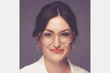 Porträt einer Person mit Brille und weißen Hemd vor neutralem Hintergrund.