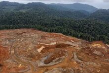 Excavators gather soil containing nickel ore at a mining site, hills with tropical forest in the background.