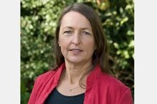 Person mit langen Haaren blickt ernst in die Kamera, Porträt im Freien vor unscharfem Grün.