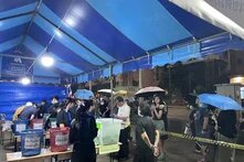 Ein blaues Zelt mit Wahlurnen, Menschen geben ihre Stimme ab.