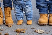Füße von zwei Erwachsenen und einem Kind. Alle haben Jeans und braune Schuhe an.