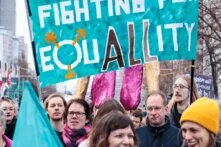 Frauen und Männer bei einer Demonstration mit einem Banner mit der Aufschrift Fighting for Equality