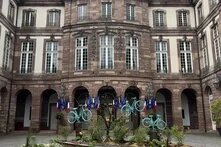 Innenhof mit historischem Gebäude; vor Bögen stehen Flaggen. In der Mitte runde Beetfläche mit mehreren aufgestellten Fahrrädern.