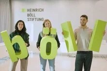 Drei nebeneinander stehende Personen halten grüne Buchstaben in den Händen - böll