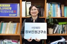 Yeo-Kyeong Chang, Executive Director of the Institute for Digital Rights holding a poster with korean lettering in front of a bookshelf.