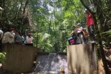 Mehrere Menschen stehen auf Betonwänden im Wald über einem kleinen Wasserlauf mit Staustufe.