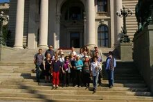 Etwa 20 Personen stehen auf einer breiten Freitreppe vor einem repräsentativen Gebäude mit hohen Säulen und posieren für ein Gruppenfoto.
