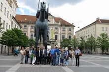 Etwa 15 Personen stehen vor einer großen Reiterstatue auf einem Platz, im Hintergrund historische Gebäude und Bäume.