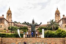 Statue von Nelson Mandela vor den Union Buildings in Pretoria, mit Gartenanlage, Menschen und zwei markanten Türmen im Hintergrund.