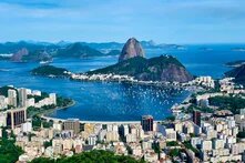 Blick über Rio de Janeiro mit Zuckerhut, Bucht voller Boote, Hochhäusern und bewaldeten Hügeln bis zum Meer.