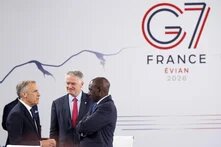 Drei Männer im Anzug sprechen vor einer Wand mit G7-Logo und der Aufschrift „FRANCE EVIAN 2026“.