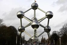 Atomium in Brüssel mit verbundenen Metallkugeln, von Bäumen gesäumter Allee und bewölktem Himmel.