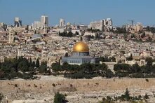 Blick über Jerusalems Altstadt mit dem Felsendom im Zentrum, Stadtmauer, Bäumen sowie dicht bebauten Wohn- und Hochhausvierteln.