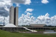 Modern government building with two tall towers and flat domed structures under a blue, cloudy sky.